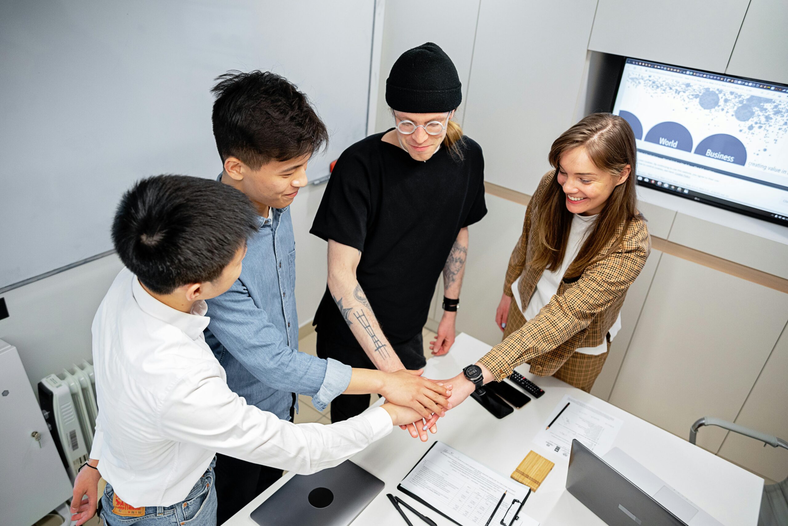 A diverse team joins hands in an office setting, symbolizing teamwork and collaboration.